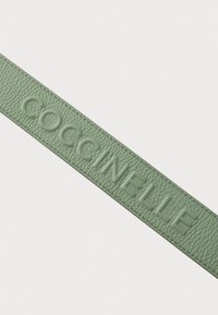 Bracelet en cuir vert avec le texte "COCCINELLE" en relief, surface texturée et couture soignée sur les bords. Design simple et minimaliste.