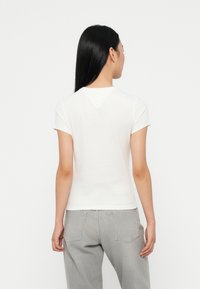 Hvit bomull t-skjorte med korte ermer, et tettsittende design og en V-formet detalj ved halsen, kombinert med lyse grå denimbukser.