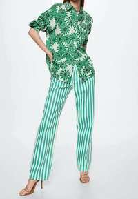 Camicia a maniche corte con stampa floreale verde abbinata a pantaloni a palazzo a righe verdi e bianche. I materiali sembrano leggeri con una vestibilità casual.