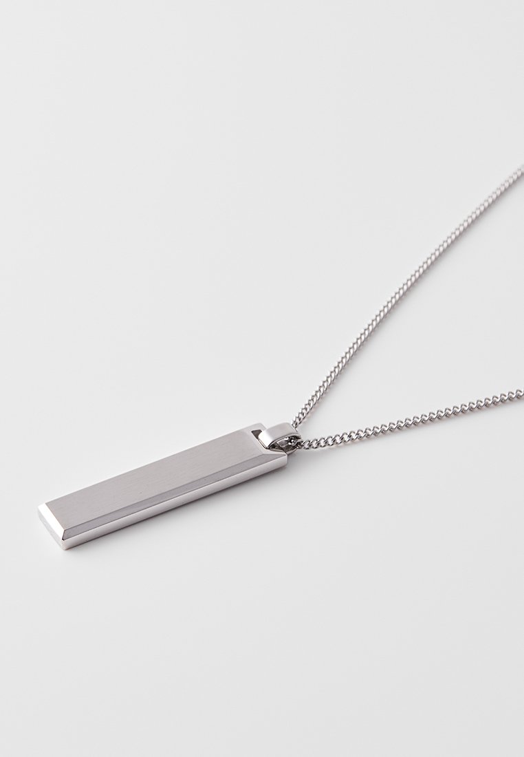 Silberner Metallanhänger an einer feinen Kette, mit rechteckiger Form, glatter Oberfläche und abgerundeten Kanten. Minimalistisches Design.