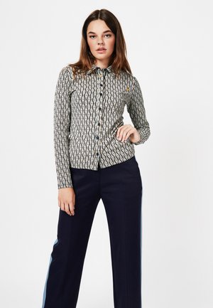 Camisa de manga larga con un patrón geométrico en crema y azul marino, con un diseño de botones y un cuello puntiagudo. Pantalones oscuros con acentos laterales claros.