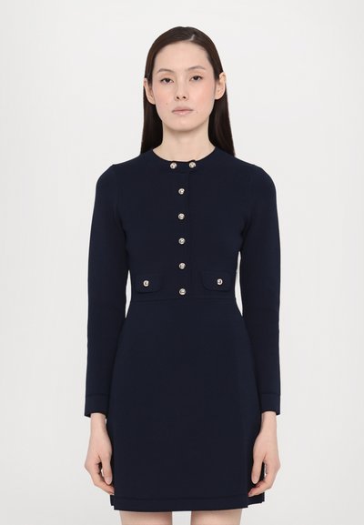 Navy blue dress with long sleeves, round neckline, front button closure, and two small pockets with flaps, made from a smooth fabric.