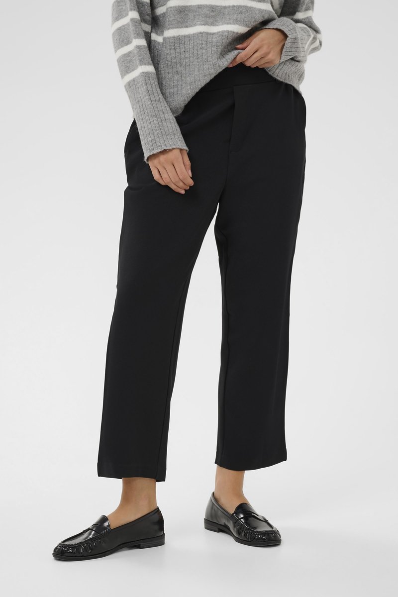 Pantalons noirs ajustés avec une texture lisse, dotés de poches latérales et d'une coupe décontractée. Associés à des mocassins noirs brillants et un pull rayé gris.