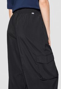 Black cargo pants with a lightweight, smooth texture. Features elastic waistband and side pockets. Simple design with no visible patterns.