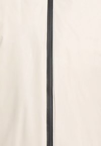 Beige stof met een zwarte verticale rits, geaccentueerd met rode stiksel langs de rand. Soepele textuur, minimalistisch ontwerp.