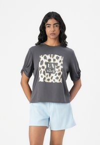 T-shirt gris à manches courtes avec un graphique imprimé léopard présentant "LA vibes" en noir. Associé à un short bleu rayé clair.