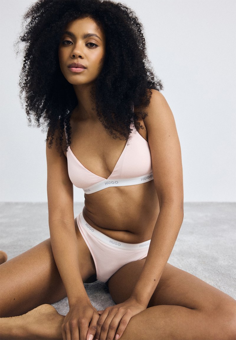 Light pink lingerie set featuring a bralette and matching briefs with a white band labeled "HUGO." Soft fabric and smooth texture.