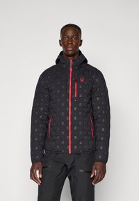 Black puffer jacket with a patterned texture, red zippers, and logo detail on the chest. Features a hood and zippered side pockets.