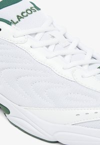 Vit atletisk sko med ovandel i mesh och syntetiskt läder, grön branding, runda snören, vadderad krage och texturerad såldetalj.