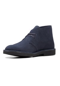 Botines de ante azul marino con punta redondeada, cierre con cordones y suela de goma negra en contraste. Presenta detalles de costura a lo largo del borde.