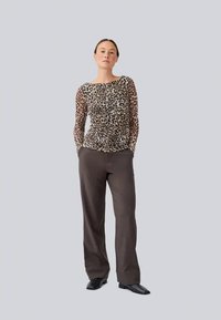 Leopard print long-sleeve top in sheer fabric, paired with dark brown tailored pants and black shoes, creating a fitted silhouette.