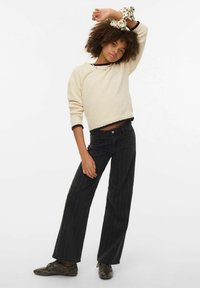 Jersey texturizado de color crema con ribete negro, combinado con vaqueros de pierna ancha de rayas negras. Modelo lleva una goma de pelo estampada en la muñeca.