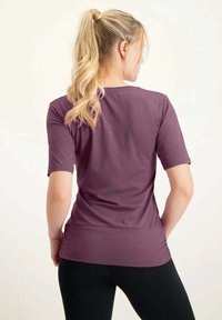 Lyhythihainen purppuranvärinen toppi, joka on valmistettu pehmeästä materiaalista, kapea malli, kaareva helma ja sileä pinta, yhdistettynä mustiin legginseihin.