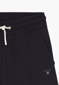 Navy sweatpants with a drawstring closure, ribbed waistband, side pockets, and a small embroidered logo on the left thigh.