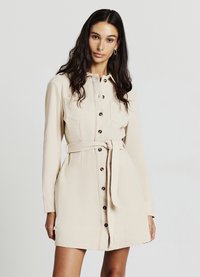 Beiges Cordhemdkleid mit Kragen, langen Ärmeln, durchgeknöpftem Vorderteil und einem gebundenen Taillendetail. Verfügt über zwei Brusttaschen und strukturierte Stoffoberfläche.