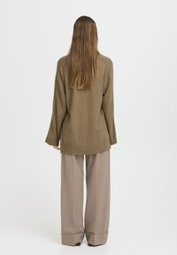 Suéter de gran tamaño en verde oliva con puños y dobladillo acanalados, combinado con pantalones de pierna ancha en beige con dobladillo doblado.