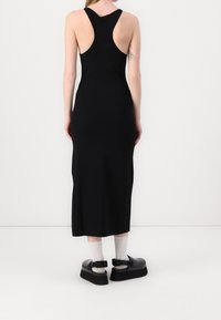Robe midi noire sans manches avec une silhouette ajustée, un dos nageur et une texture lisse, assortie à des chaussures plateformes noires épaisses et des chaussettes.