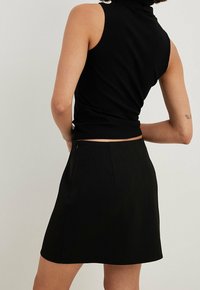 Top sans manches noir à côtes associé à une mini-jupe noire. La jupe a une texture lisse et une fermeture éclair discrète à l'arrière.