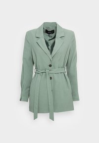 Blazer verde chiaro con vita cintrata, colletto a rever e maniche lunghe. Presenta tre bottoni frontali e un tessuto dalla texture particolare.