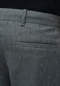 Κοντινή λήψη ενός γκρι υφασμάτινου παντελονιού με υφή, εστιασμένη στην πίσω τσέπη και τη μέση με θηλιά για ζώνη.