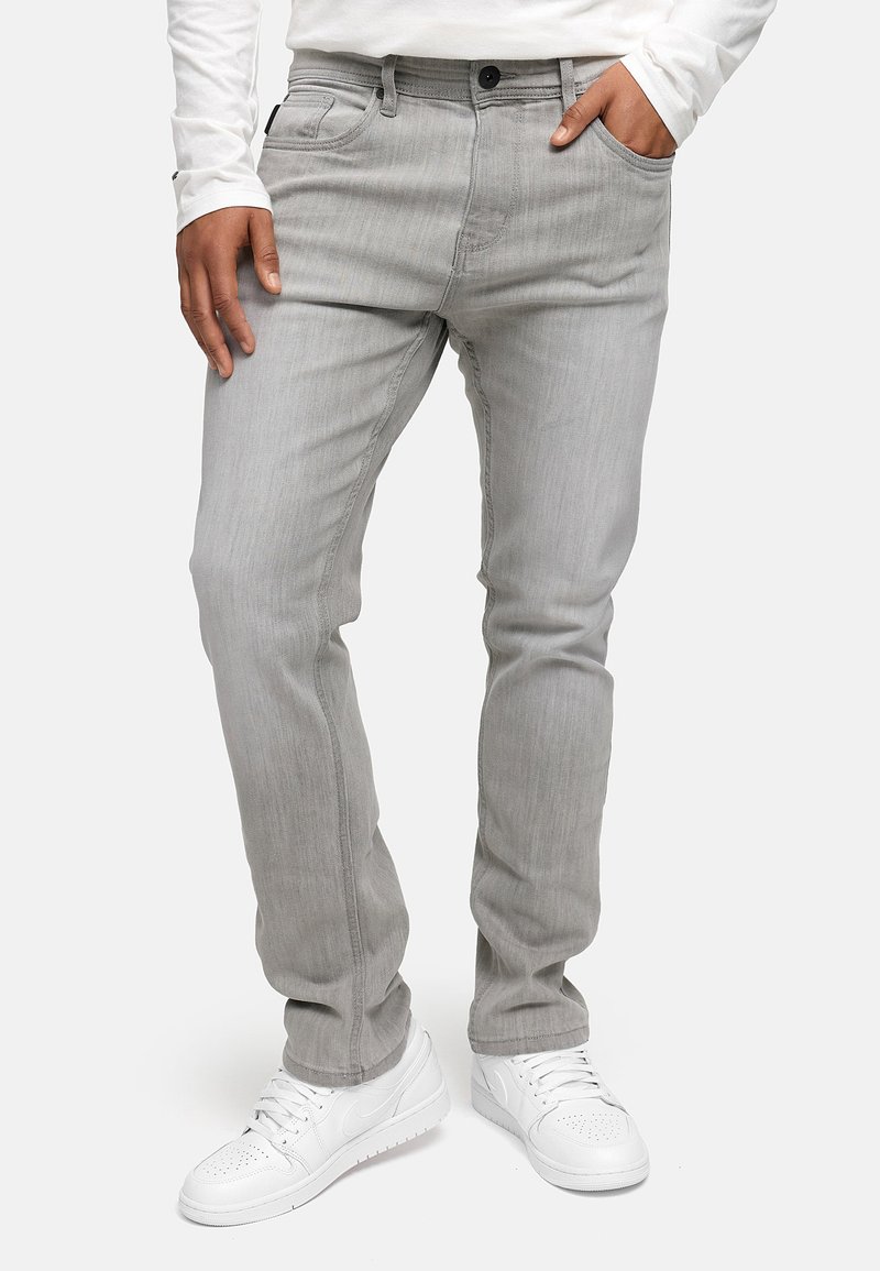 Jean gris clair en denim, présentant une coupe droite, cinq poches et une texture subtile. Assortis à des baskets blanches.