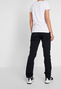 Camiseta blanca de algodón con mangas cortas y un diseño circular en la espalda, combinada con pantalones negros ajustados y zapatillas negras y blancas.