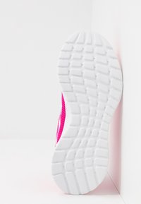 Suela de goma blanca con un patrón de diseño texturizado de una zapatilla deportiva rosa apoyada contra una pared blanca de esquina.