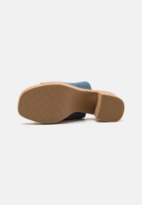 Scarpa in tessuto blu con suola in gomma testurizzata, caratterizzata da un design a motivi e dettagli antiscivolo. La scarpa ha un tacco basso e una forma arrotondata.