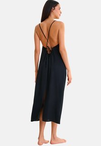 Robe maxi noire avec des bretelles spaghetti et un dos nu. Présente une taille cintrée, une fente sur le côté et un détail à nouer à l'arrière. Texture lisse.