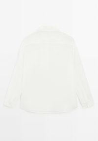 Camicia bianca a maniche lunghe realizzata in un tessuto liscio. Presenta un colletto classico, polsini con bottone e una linea dritta con un orlo leggermente curvato.