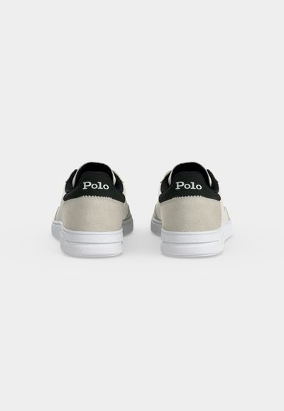 Pereche de adidași bej și negri cu tălpi albe, văzuți din spate, cu branding "Polo" pe etichetele negre de pe călcâi.