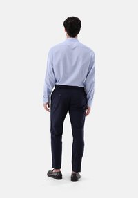 Camicia a quadri azzurra chiara con maniche lunghe e polsini con bottone, abbinata a pantaloni aderenti blu navy, scarpe nere e una finitura liscia.