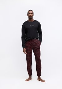 Schwarzes Langarmshirt mit "HUGO"-Aufdruck, kombiniert mit rot karierten Hosen mit elastischem Bund und Knöchelbündchen.