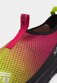 Κοντινό πλάνο πολύχρωμου επάνω μέρους παπουτσιού από πλέγμα σε κίτρινες, πορτοκαλί και ροζ αποχρώσεις με μαύρη σόλα και υφασμάτινη θηλιά στην φτέρνα.