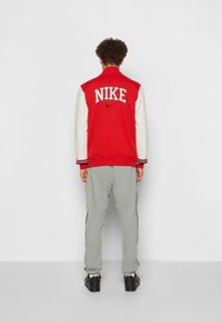Red and white Nike varsity jacket with embroidered logo; gray sweatpants with side stripes; black sneakers; soft, textured fabric.