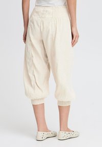 Pantalons croppés beige clair avec une taille élastique, des poignets froncés et un tissu doux et texturé. Présente des détails minimaux à l'arrière.
