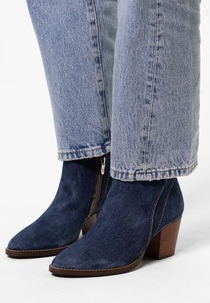 Denim enkellaarsjes met een puntige neus, zijrits en een bruine houten hak. Gepaard met licht gewassen, iets versleten jeans.