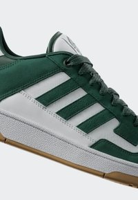 Zelene i bijele atletske tenisice koje su izrađene od suede i kože. Imaju tri bijele pruge, teksturiranu bijelu potplatu i sive vezice.