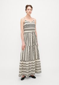 Rochie maxi cu model alb și negru, cu bretele subțiri, design în straturi și talie ajustată, asortată cu balerini negri.