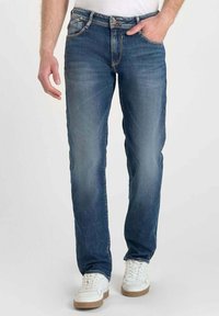 Jean en denim bleu avec une coupe droite, arborant un design classique à cinq poches et des coutures contrastées. Portés avec des baskets blanches et une chemise unie.