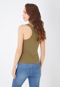 Camiseta sin mangas color verde oliva en algodón suave, con un diseño de espalda redondeada y forma ajustada, combinada con jeans de mezclilla azul claro.