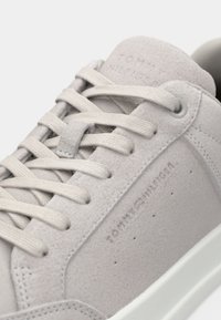 Light gray suede sneaker with tonal laces, embossed "Tommy Hilfiger" logo on the side and tongue, and white rubber sole.