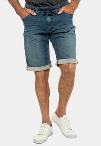 Bermudas de denim en azul oscuro con dobladillo vuelto, que presentan una cintura con cordón, bolsillos y una textura suave. Combinadas con zapatillas blancas.