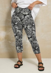 Svart och vit capri leggings med ett fjärils mönster, hög midja och mjukt, stretchigt tyg. Bärs med svarta platta sandaler.