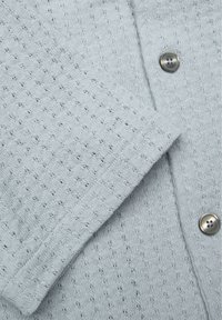 Lichtgrijze gebreide trui met een gestructureerd, open steekpatroon. Voorzien van een ronde halslijn en zilverkleurige knoopaccenten. Zacht, ademend materiaal.