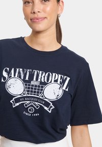 T-shirt en coton bleu marine avec un graphique de tennis vintage blanc et du texte, col rond et manches courtes. Texture lisse.