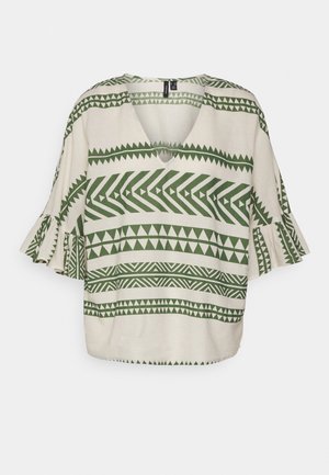 Kremowa bluzka z zielonymi geometrycznymi paskami i wzorami w kształcie trójkątów, z dekoltem w serek i rozkloszowanymi rękawami o długości do połowy przedramienia.