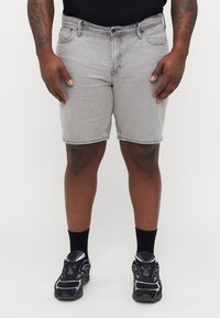 Grijze denim shorts met een normale pasvorm, voorzakken en een knoopsluiting, gecombineerd met zwarte sportschoenen en zwarte sokken.