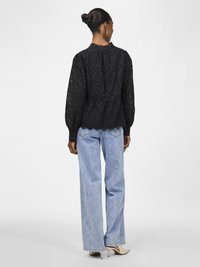 Black lace blouse with puffed sleeves, high neckline, and decorative stitching. Paired with light blue wide-leg jeans and nude heels.