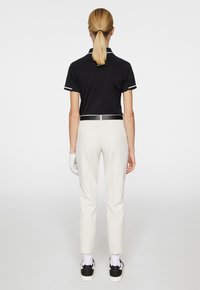 Black polo shirt with white accents, paired with light beige textured pants. White golf glove and black sneakers complete the outfit.